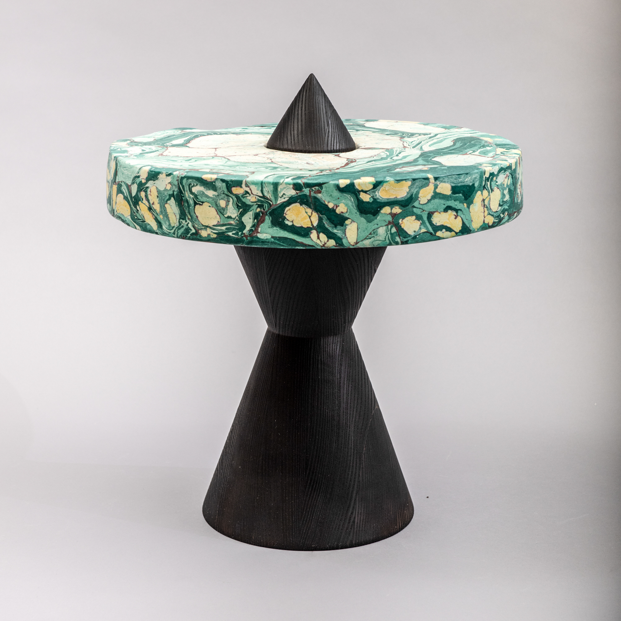 General Life's "Pickle" Table consists of three stacked cones in turned, ebonised ash with an etched brass foot insert, supporting on its shoulders a scagliola ring – the colors and patterning of which is inspired by the designer’s love for sour Polish pickles. Front view.