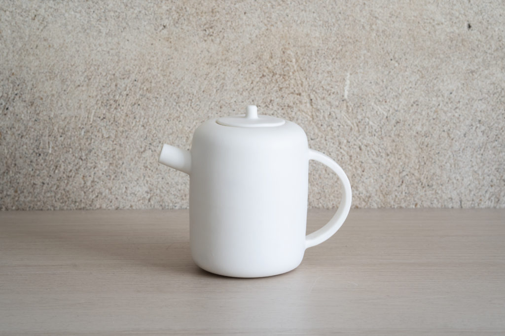 Silent teapot with a pale minimal body and slim spout on a plain surface