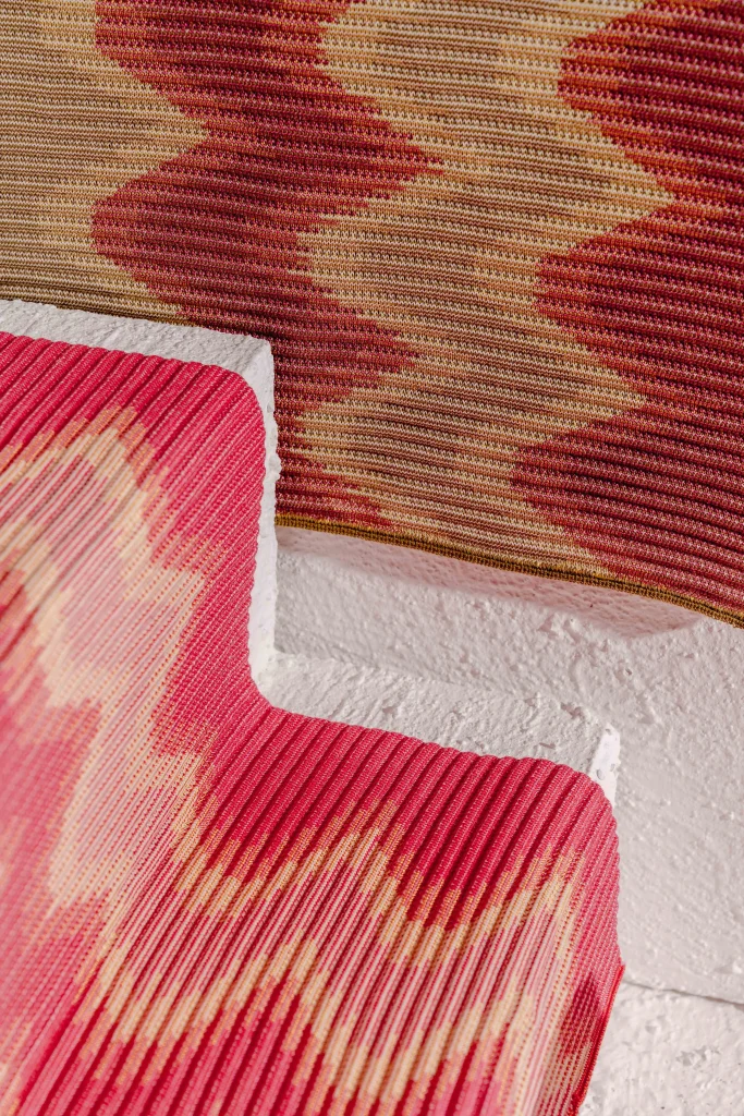 Two BOI table mats layered on white stone, showing the zigzag weft pattern in reds and cream