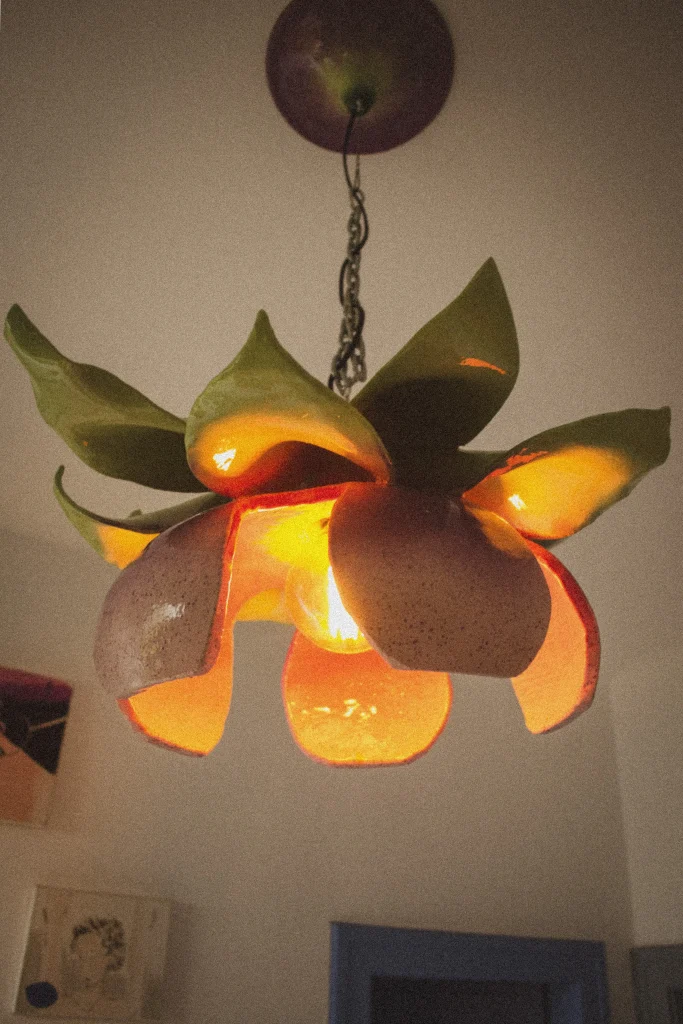 Amaryllis ceiling lamp with glazed ceramic petals in green, orange and pink opening around a warm light, by UAU Studio