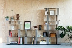 Stack 021 modular raw aluminum shelving wall holding books, records and objects against a plywood wall by studio MOTO