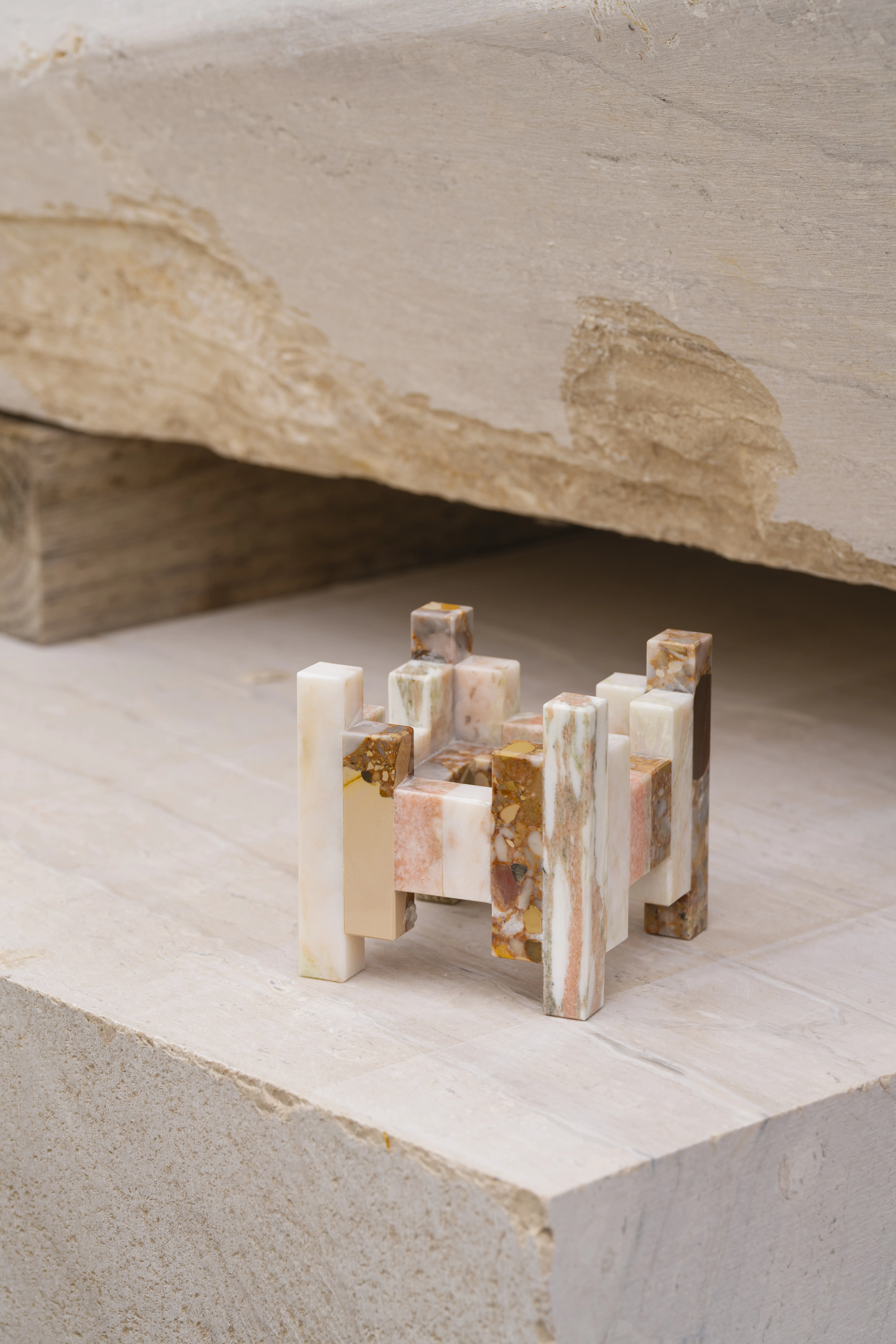 Strata flower vase built from slender pink, white and amber marble offcuts stacked in a staggered grid, set on a block of raw stone, by Iyo Hasegawa