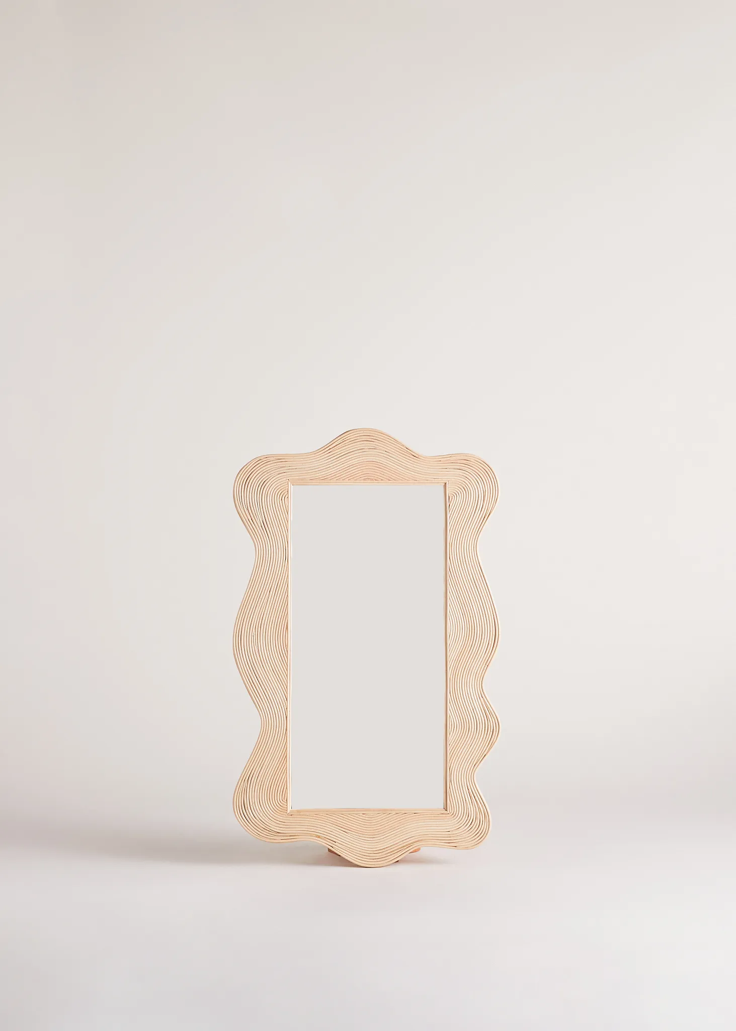 Sofia statement wall mirror with a natural rattan frame carved into an undulating wave by Heaps & Woods