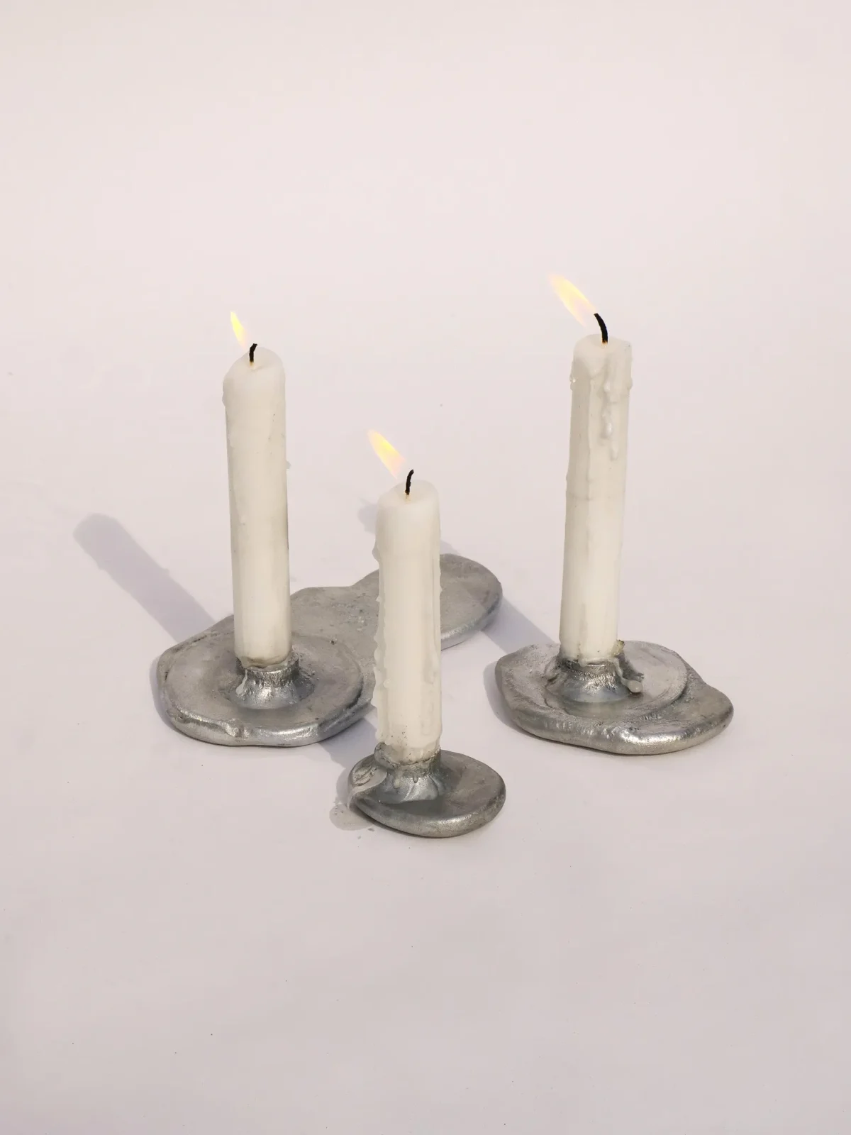 Group of sandcast candleholders in metal, surfaces left raw from the mould
