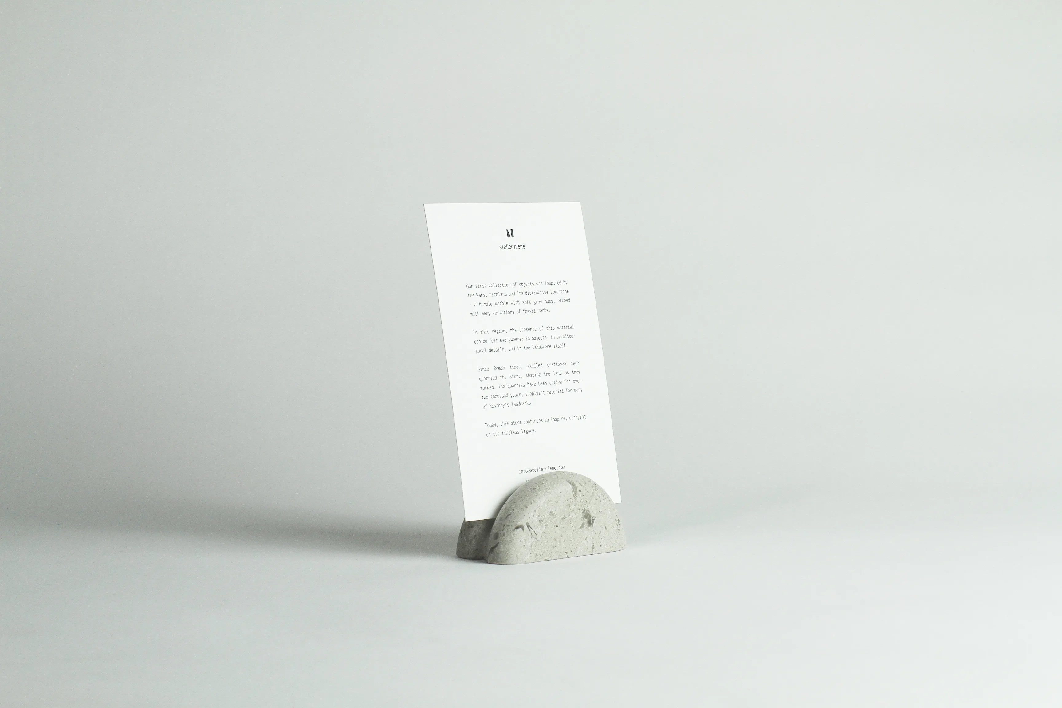 Iste photo holder, a small rounded block of fossil-flecked Lipica limestone holding an upright printed card, by Atelier Nienē