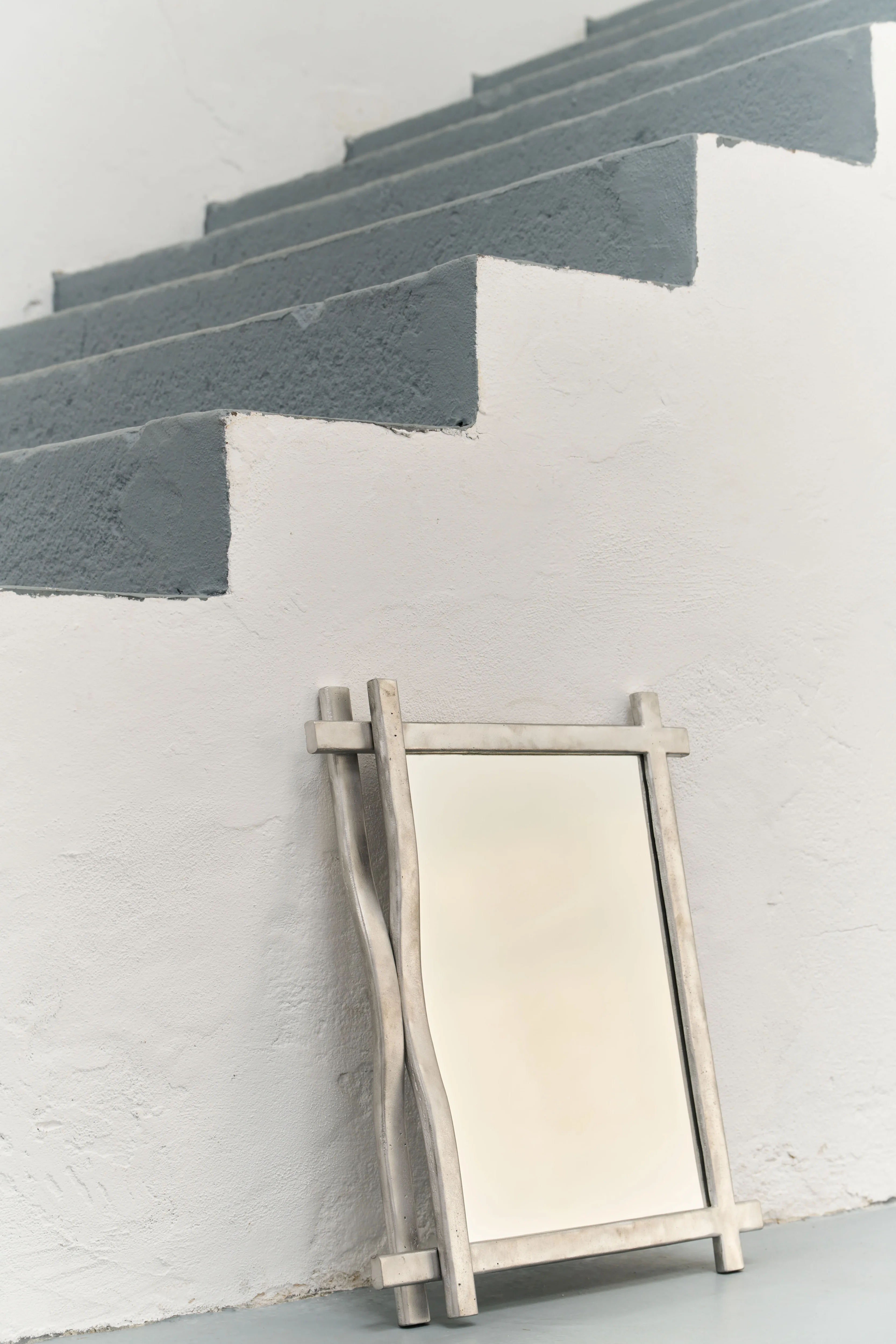 Trama mirror in cast aluminum with intertwining linear frame