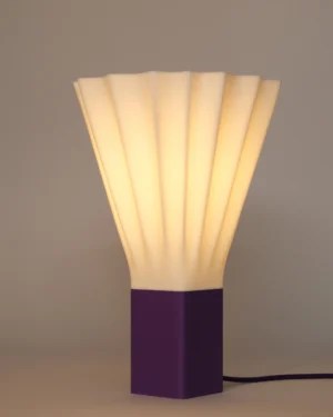 Plissé Mini Table Lamp in Jade White bio-plastic with an Iris Purple base, on a table.