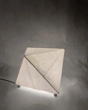 Biiit 006 Table Lamp in faceted paper and brass on a table, front view.