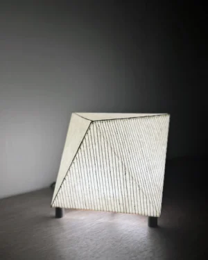 Biiit 007 Table Lamp in faceted paper and brass on a table, front view.
