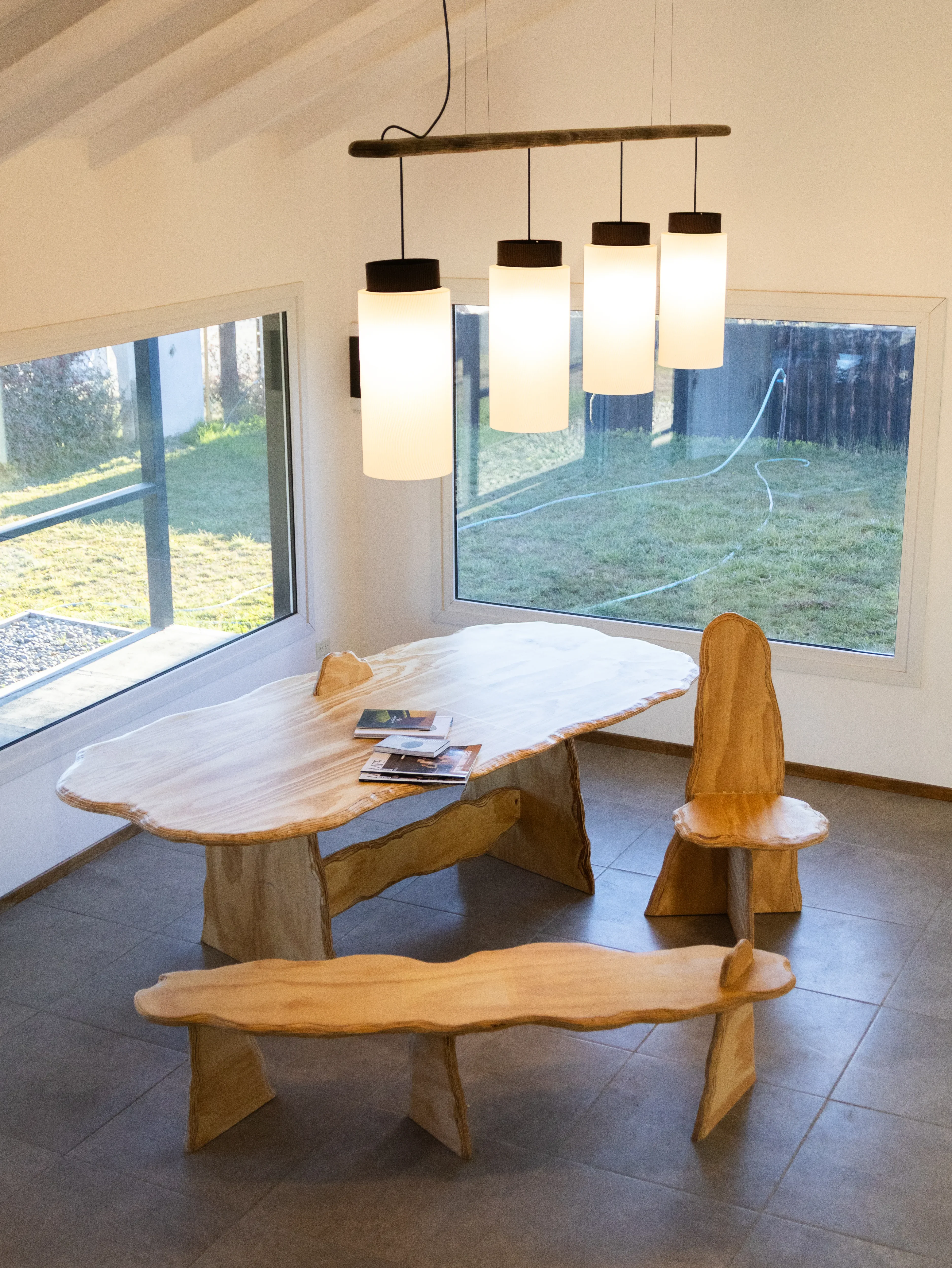 Estratos dining table in laminated plywood with organic curved edges showing its layers, with a matching bench, in a bright room, by Aldo Montes de Oca