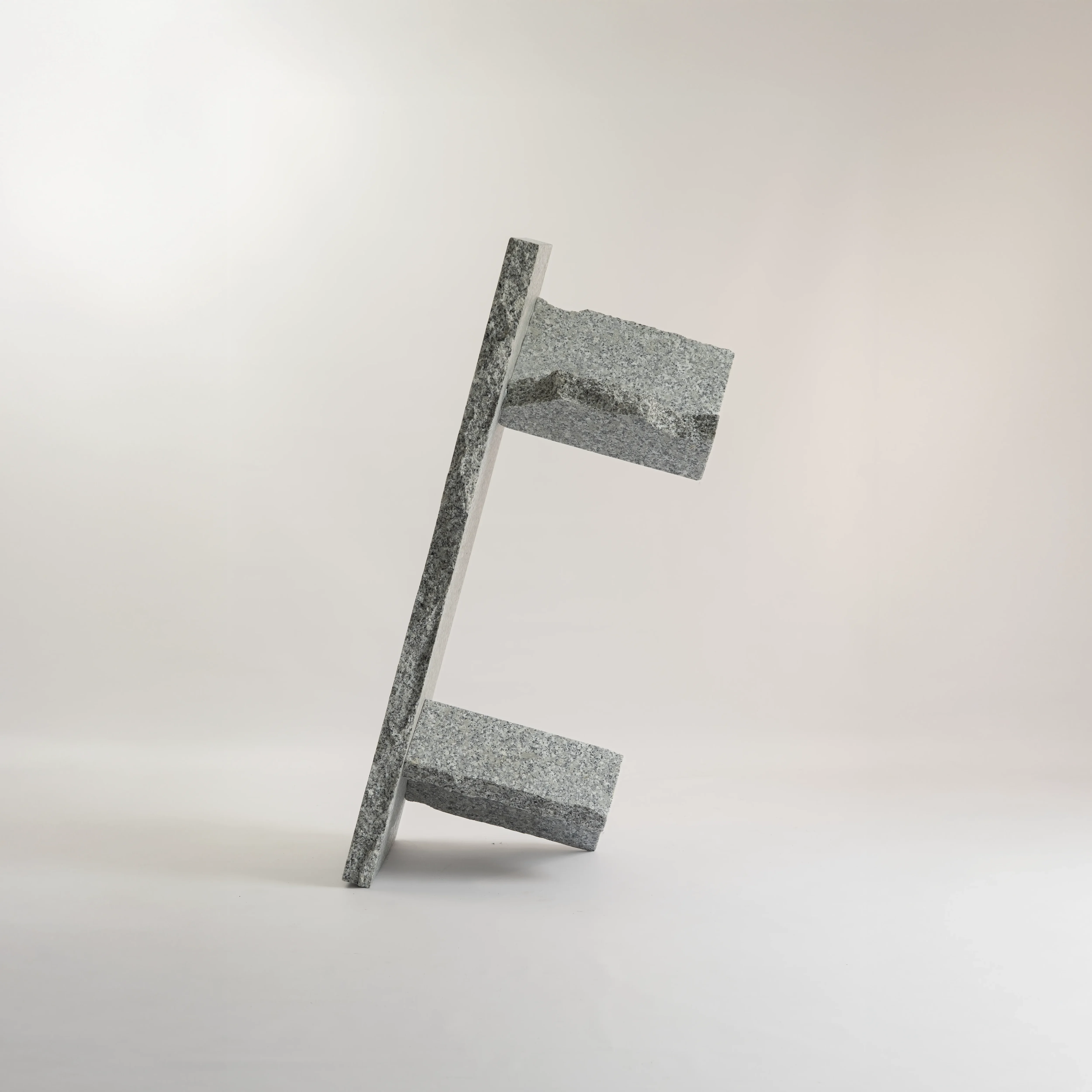 Filar bench in rough-split gray Strzegom granite shown standing on its end, revealing the slab top and two block legs, by małe dobra
