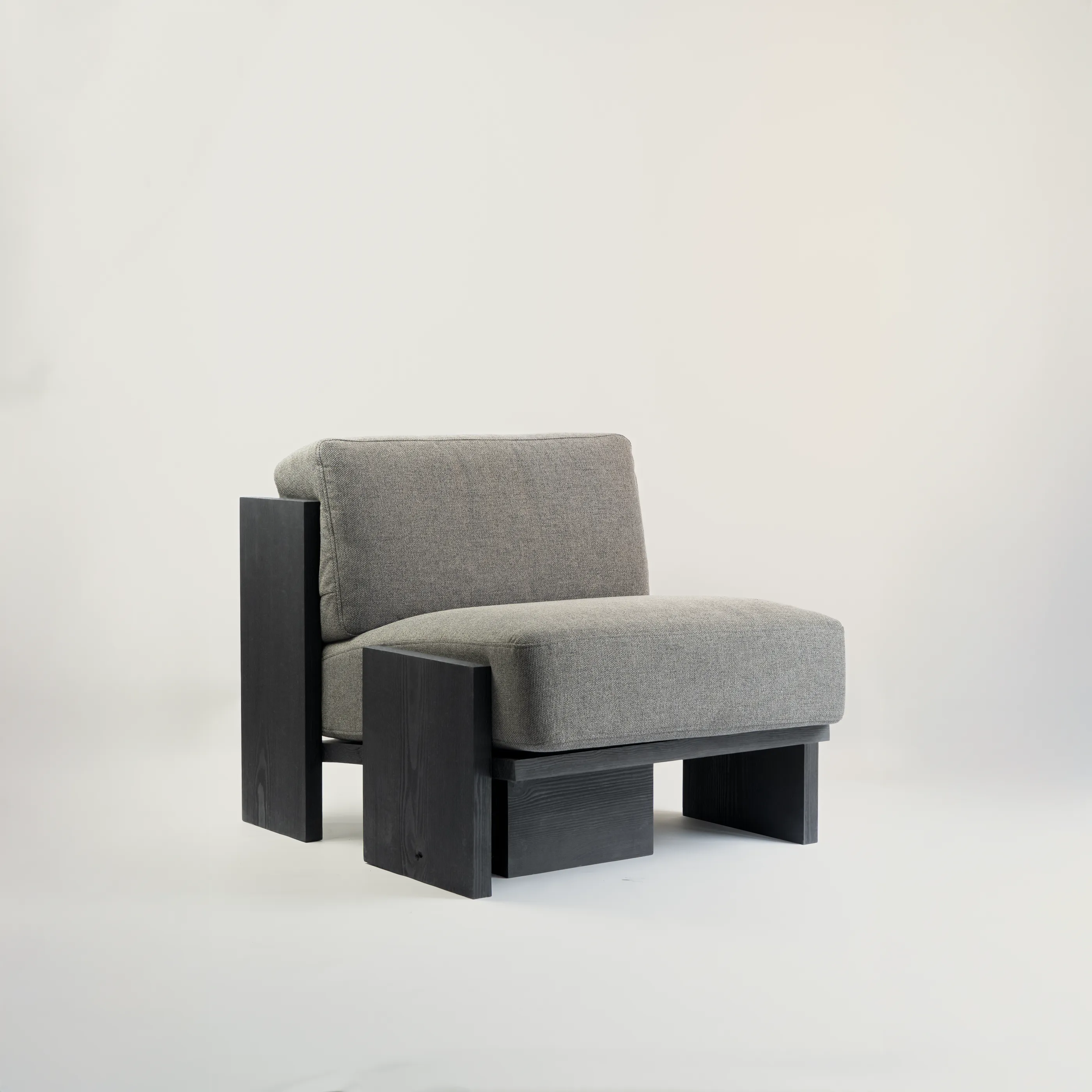 Brut lounge chair with a dark solid pine frame of thick slabs and a gray upholstered seat and back, on a pale background, by małe dobra