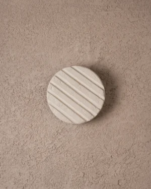 Wilo Fluted Egg White Wall Sconce in off-white clay with diagonal fluting on a textured wall, front view.