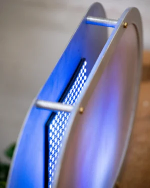 Cumulo Table Lamp in silver aluminum with a blue glowing glass panel on a wooden surface, angled view.