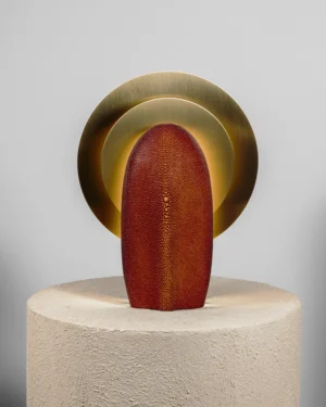 Mother of the Light Édition Cognac Table Lamp in amber-red galuchat with brass discs on a stone plinth, front view.