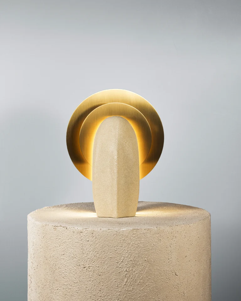Mother of the Light Table Lamp by PALUCKI Studio, lit galuchat and brass lamp on a rough cream plinth, plain grey background