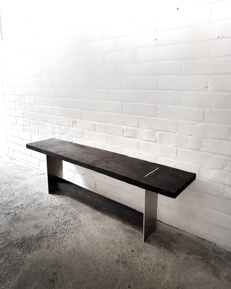 Blackwood Aluminium Bench by case studios in a room, standing on a concrete floor against a white brick wall