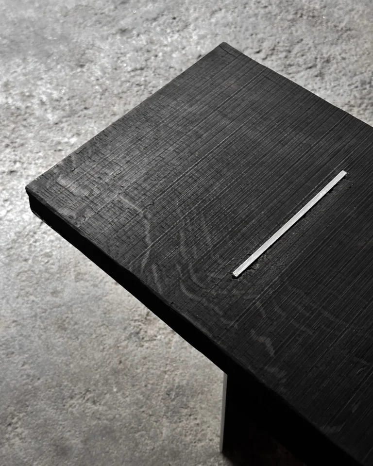 Close-up of the Blackwood Aluminium Bench's brushed black oak seat with an inlaid aluminum strip, on a concrete floor