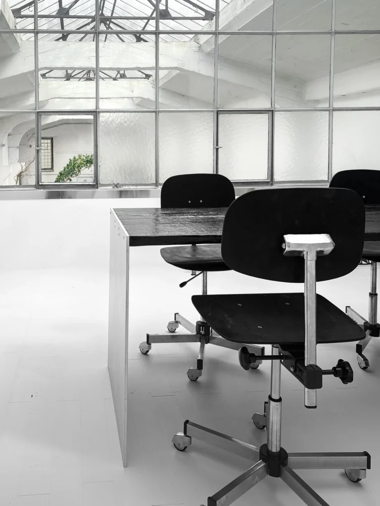Yakisugi Desk by case studios in a loft office, a black swivel chair in front and a glazed skylight roof behind