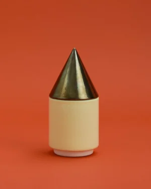 Knstrkt Set Of 2 With Large Pieces by Studio Berg, cream stoneware container with a gold cone lid, on a red background