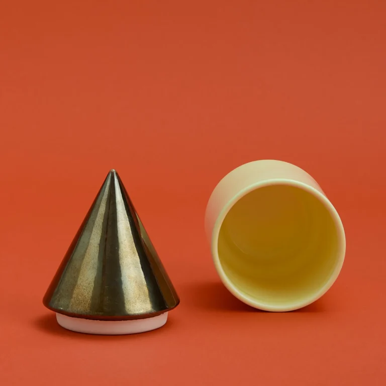 Knstrkt Set Of 2 With Large Pieces by Studio Berg, gold cone lid beside the cream container lying on its side, interior visible
