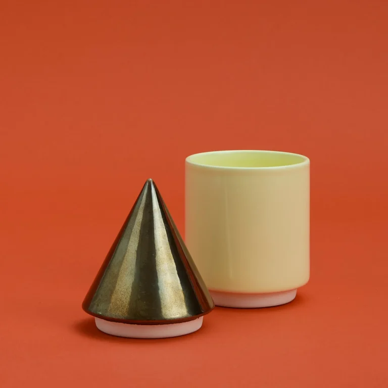 Knstrkt Set Of 2 With Large Pieces by Studio Berg, gold cone lid standing beside the open cream container, on a red background