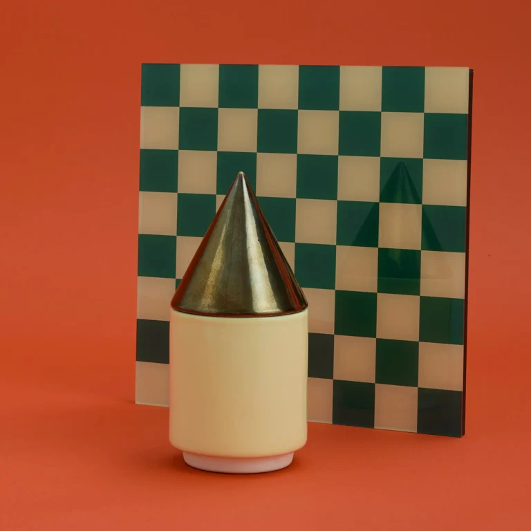 Knstrkt Set Of 2 With Large Pieces by Studio Berg, cream container with gold cone lid in front of a green and cream checkered panel