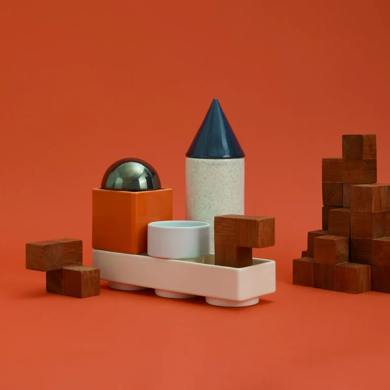 Knstrkt Set Of 6 by Studio Berg arranged among small wooden blocks, with a glossy dome lid and blue cone on orange
