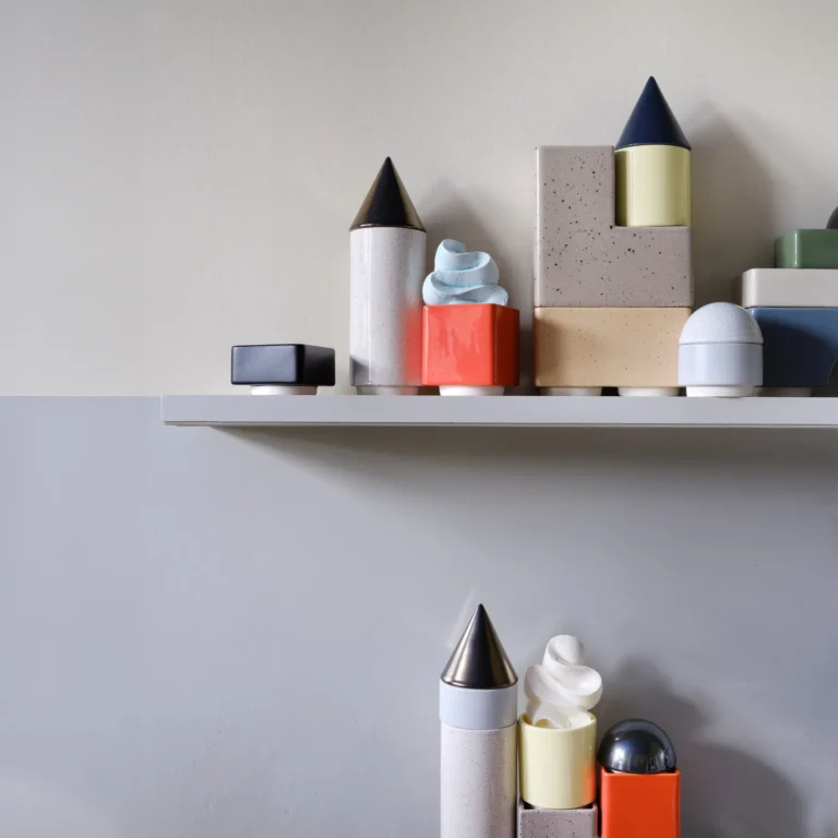 Close-up of the Knstrkt Set Of 14 by Studio Berg on a shelf, speckled blocks, cone towers and a whipped swirl on a red cube