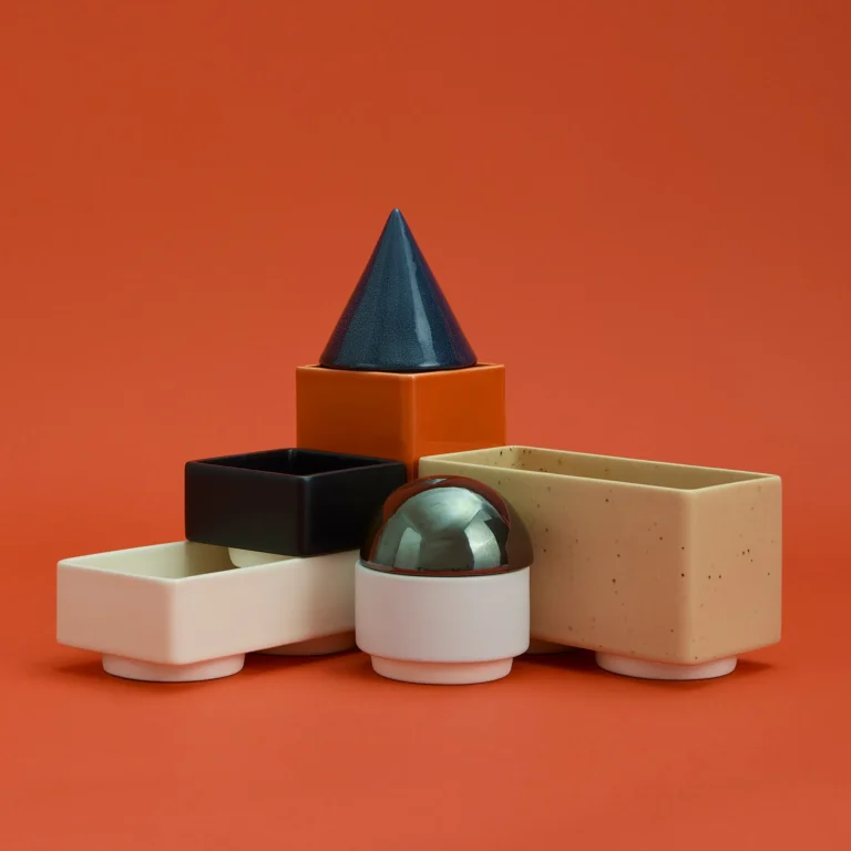 Knstrkt Set Of 7 by STUDIO BERG seen from a lower angle, a speckled beige tray beside a stacked cone, black and orange blocks