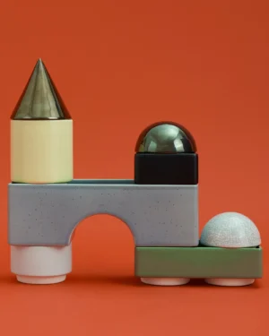 Knstrkt Set Of 8 by Studio Berg, stacked ceramic blocks in pale yellow, grey, green and black, on a plain orange background