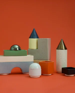 Knstrkt Set Of 14 by Studio Berg, stackable glazed ceramic blocks, cones and domes, on a plain orange background