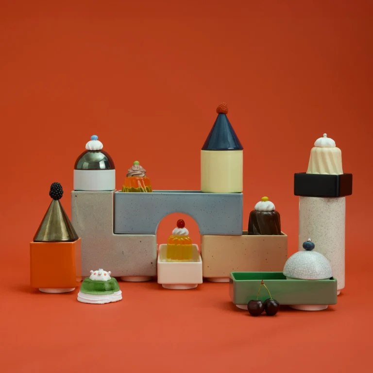Knstrkt Set Of 14 by Studio Berg topped with small sculpted sweets, cherries and berries, on an orange background