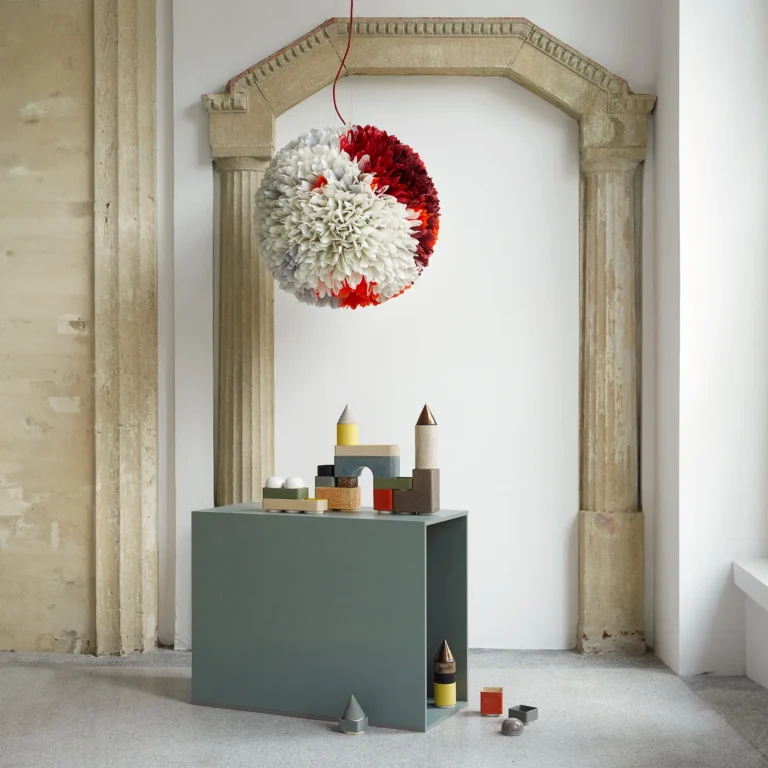 Knstrkt Set Of 14 by Studio Berg on a green cabinet in a room, beneath a round pendant of red and white feathers