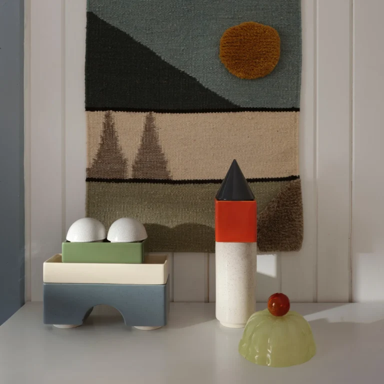 Knstrkt Set Of 14 by Studio Berg on a white shelf in front of a woven wall hanging, beside a green glass dome