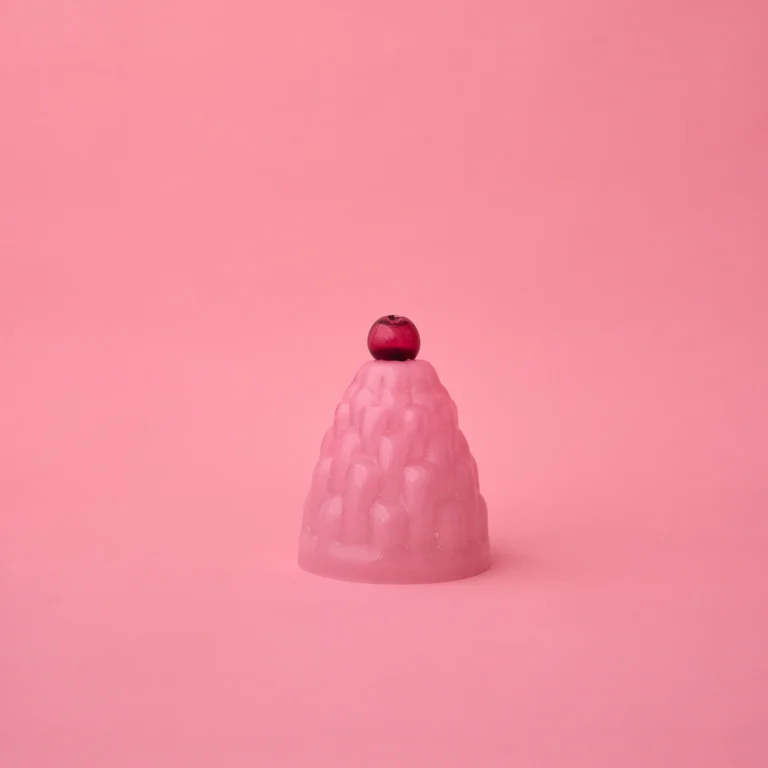 Jello High by Studio Berg, pale pink glass cloche with raised bumpy texture and a dark red knob, on pink background