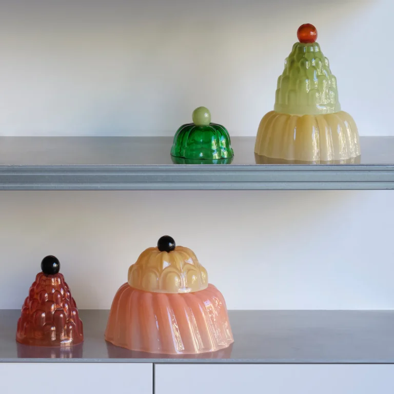 Jello High by Studio Berg on two gray shelves, glass cloches in green, cream, peach and red with round knobs