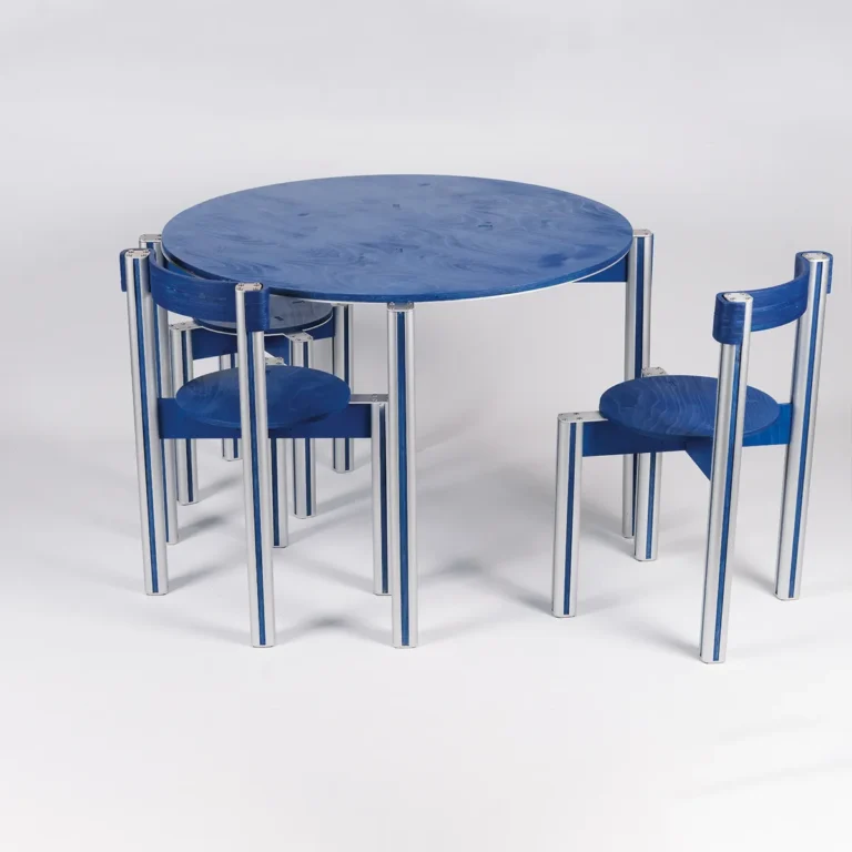 Sigma 01 Dining Table in Aluminum and Birch Plywood by 301 Design Studio seen at an angle, surrounded by blue chairs with aluminum legs