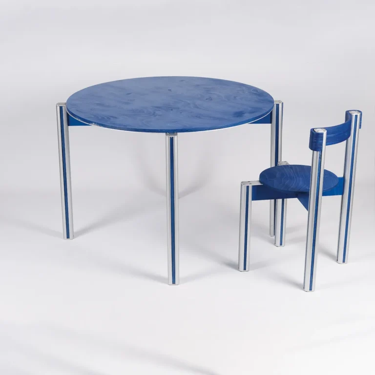 Sigma 01 Dining Table in Aluminum and Birch Plywood by 301 Design Studio beside a chair, showing blue striped aluminum legs