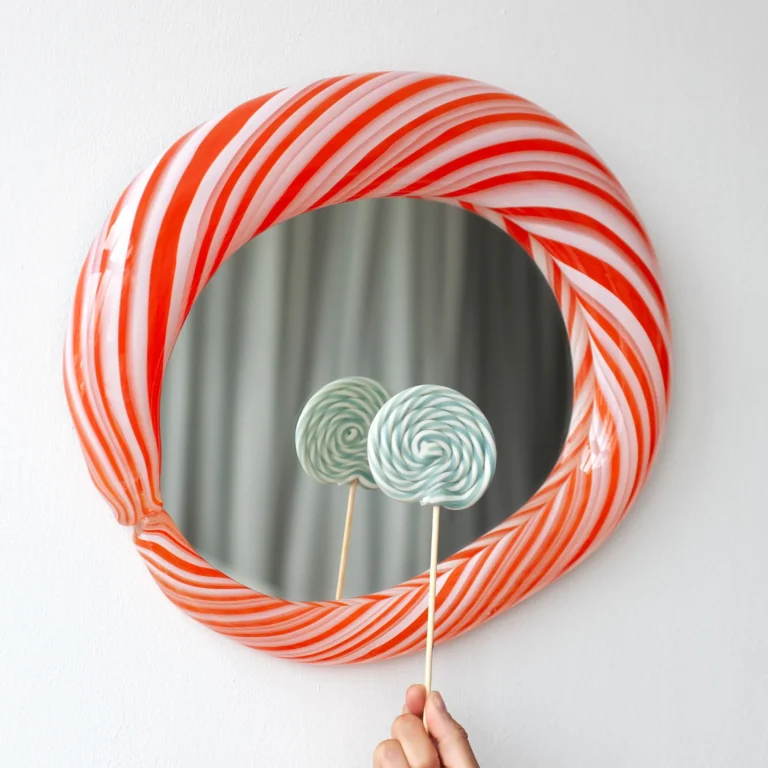 Close-up of the Red Candy Mirror's red and white striped glass frame, with a hand holding two lollipops reflected in it
