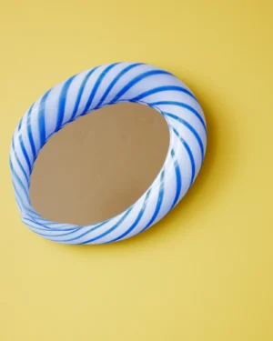 Blue Candy Mirror by STUDIO BERG, oval wall mirror in twisted blue and white striped glass, on a yellow wall