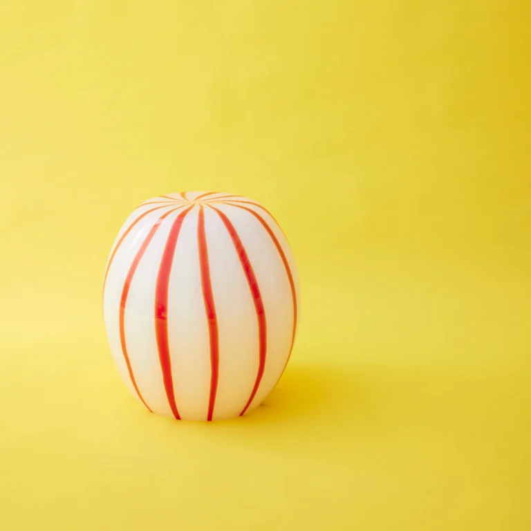 Red Candy Side Table by STUDIO BERG, white glass stool with many narrow red stripes, on a plain yellow background