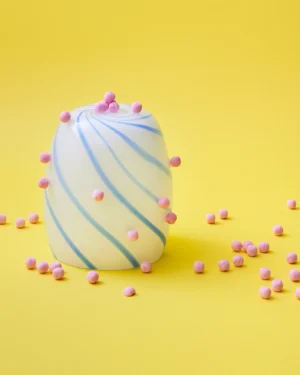 Blue Candy Side Table by STUDIO BERG, white glass table with blue swirl stripes, pink sweets scattered on yellow