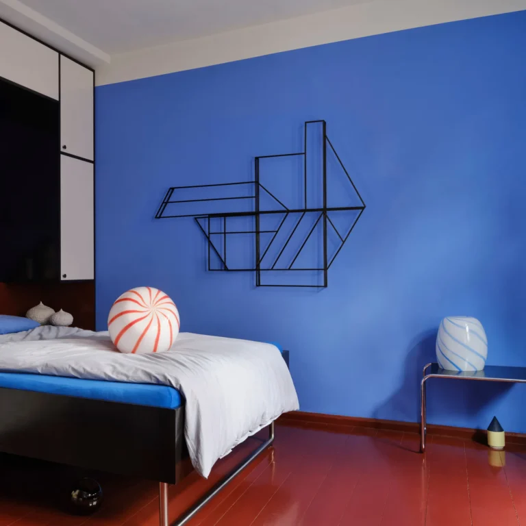 Blue Candy Side Table by STUDIO BERG in a bedroom, beside a bed on a steel side table against a blue wall
