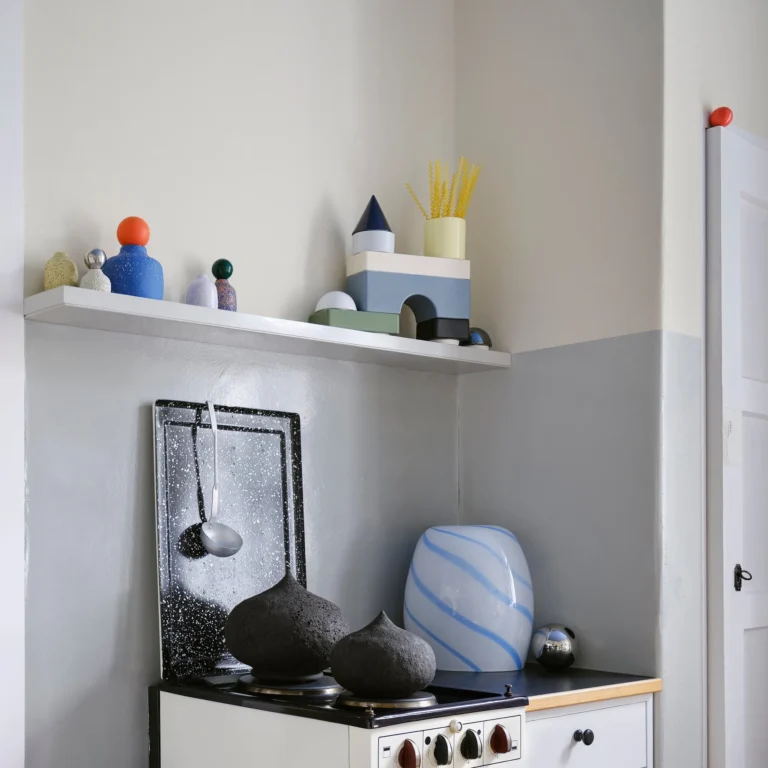 Blue Candy Side Table by STUDIO BERG in a kitchen corner, striped glass piece beside a stove under a shelf of objects