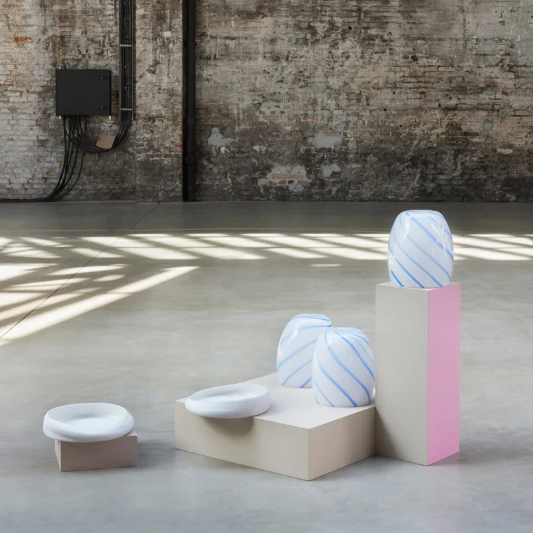 Blue Candy Side Table by STUDIO BERG in a concrete hall, striped glass pieces on cream and pink plinths beside white dishes