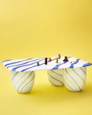 Blue Candy Sofa Table by Studio Berg, blue and white striped glass table with sweets stacked on top, on yellow