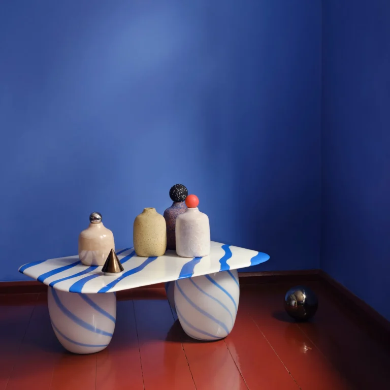 Blue Candy Sofa Table by Studio Berg in a blue corner room, with small vases and a cone on the striped top