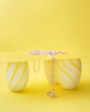 Yellow Candy Sofa Table by Studio Berg, yellow glass top on striped legs, a candy necklace draped over the edge