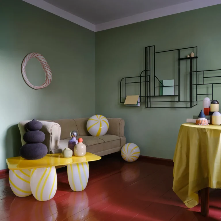 Yellow Candy Sofa Table by Studio Berg in a green living room, a dark stacked sculpture and small vases on top